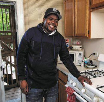 Man smiling standing in his kitchen next to the stove 