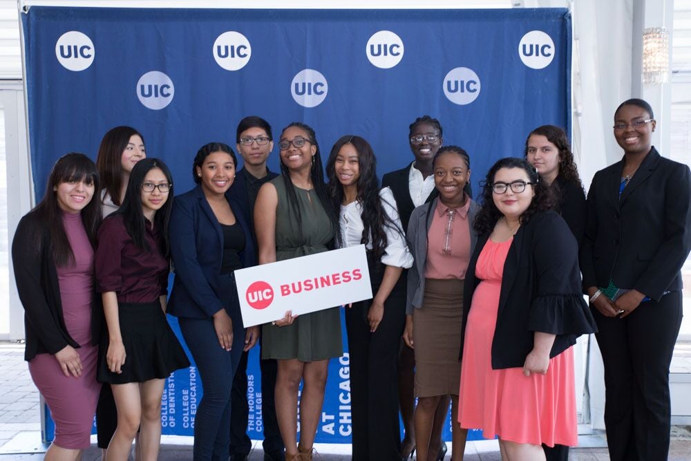 A group of students standing in front of a UIC backdrop holding a UIC Business sign