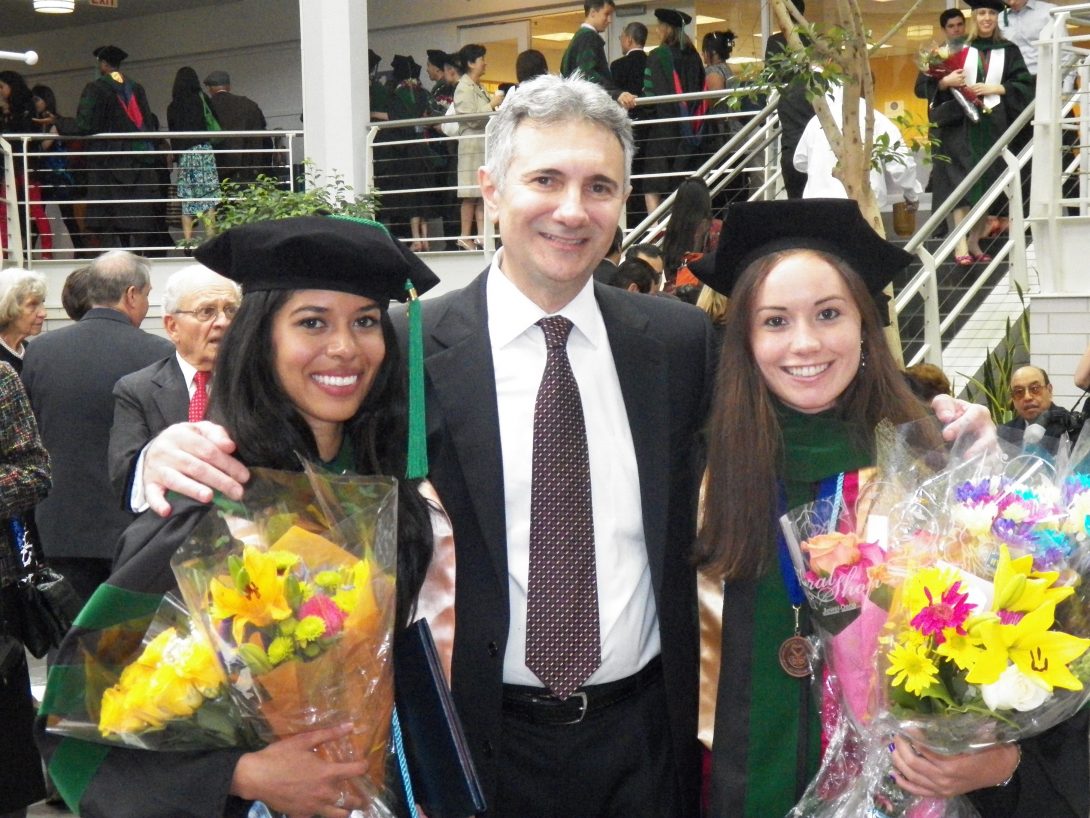Two women holding flowers in graduation gowns with one man in the middle