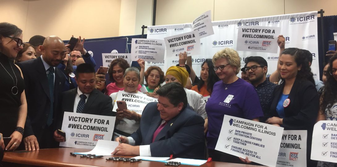 Governor Pritzker signing a document at a desk surrounded by people.