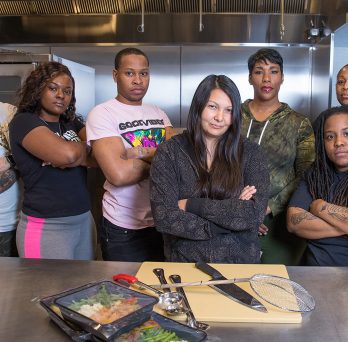 Seven people posing for the camera in a kitchen 