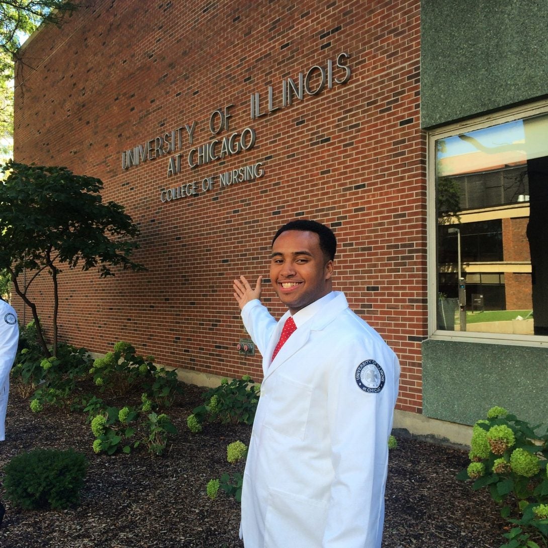 A man in a lab coat smiling and gesturing toward a building