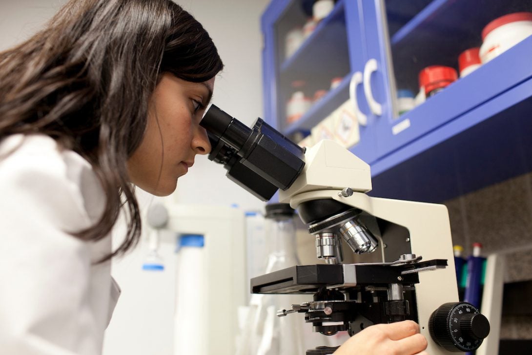 Woman in a lab coat looking through a microscope.